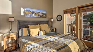 A bedroom with a bed, two bedside tables, a wall-mounted clock, and a large window with a view of the outdoors.