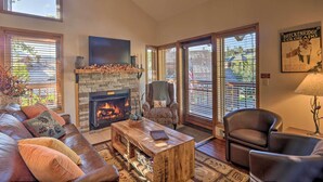 A spacious living room with a fireplace, leather sofa, and a large window with blinds.