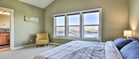 A bedroom with a large bed, a window with a view, a chair, and a small kitchen area.