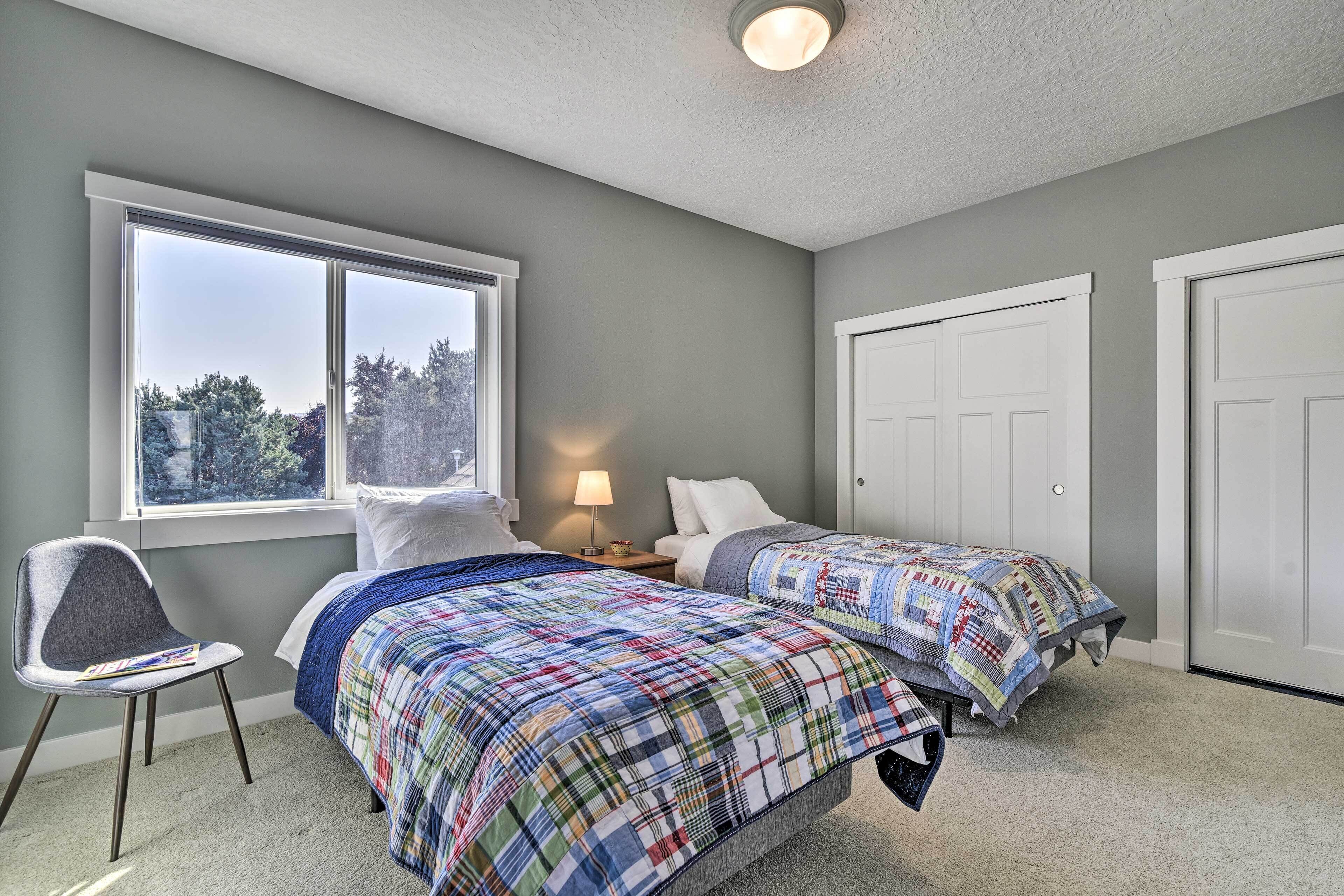A bedroom with two beds, a window, a chair, and a lamp.