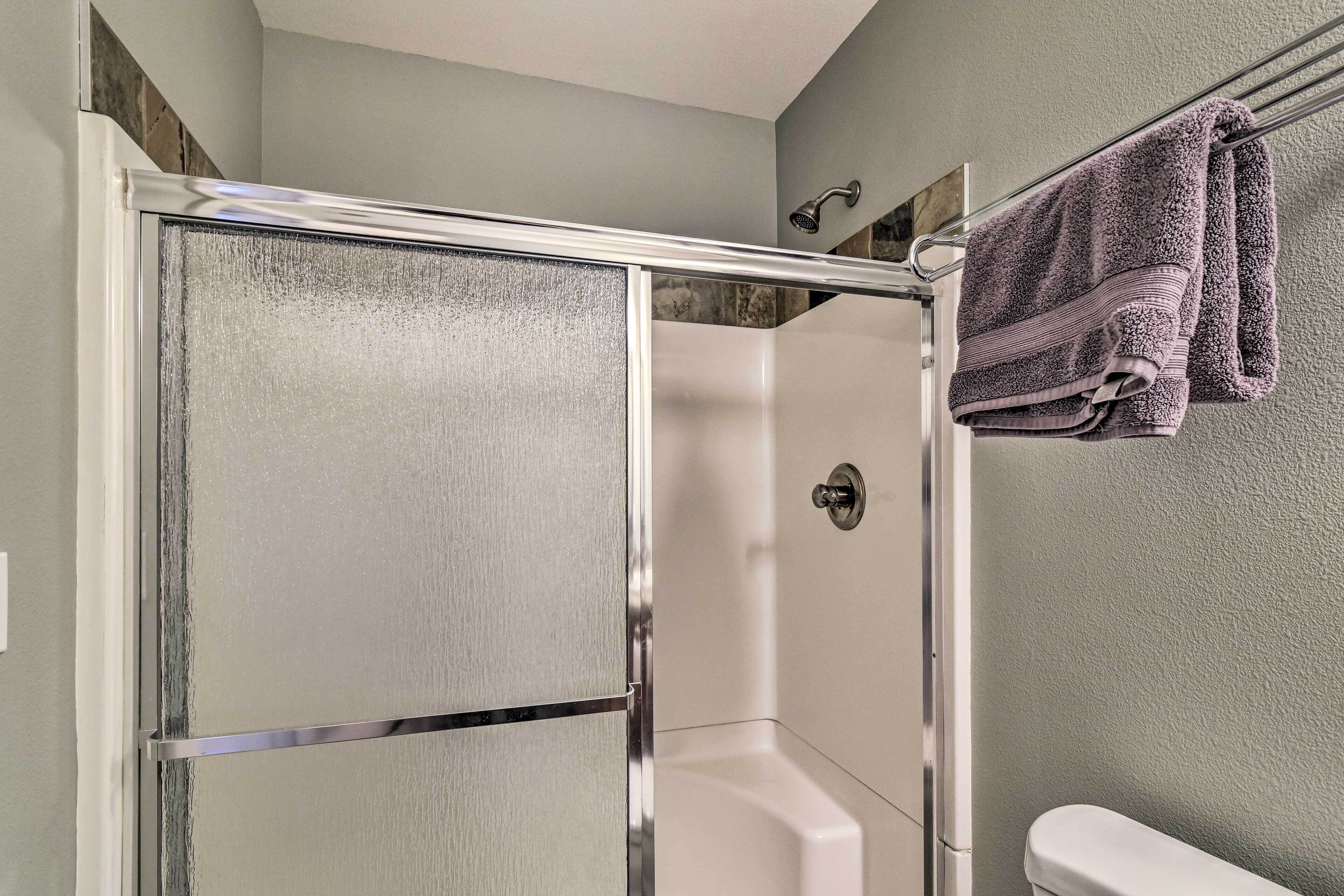 A shower enclosure with a glass door, a white bathtub, and a towel rack with a folded towel.