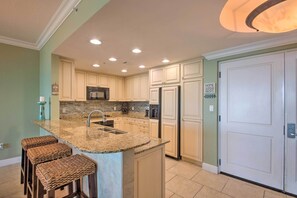 A modern kitchen with a granite island, stainless steel appliances, and light green walls.