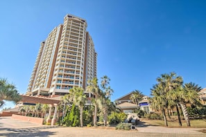 A tall hotel with multiple floors, surrounded by palm trees and a clear blue sky.