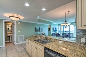 A kitchen with granite countertops, a double sink, and a dishwasher. There is a dining area visible through an open doorway.