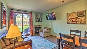 Ein Wohnzimmer mit einer Couch, einem Couchtisch, einem an der Wand montierten Fernseher, einem Kamin und einem Esstisch mit Stühlen.