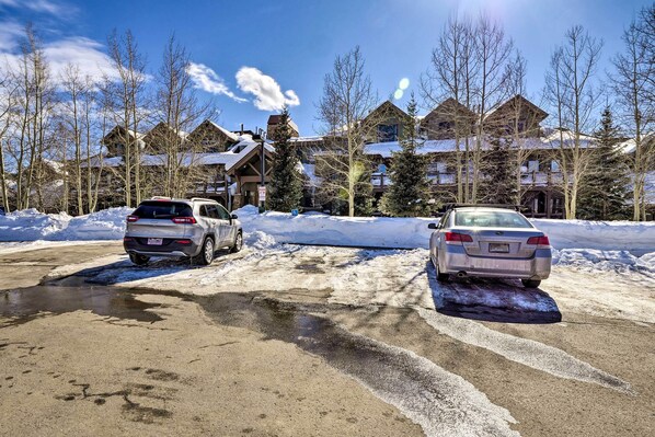 A snow-covered parking lot with two cars parked, surrounded by buildings with snow on their roofs and bare trees. - Couple's Ski Condo: 1 Mi to Breckenridge Golf Club (Breckenridge)