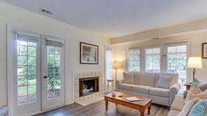 A living room with a fireplace, a sofa, a coffee table, and a view of the outdoors through large windows. - 1 Mi to Beach: Family-friendly Evian Resort Condo! (Hilton Head Island)