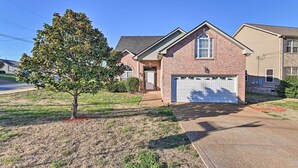 A single-story brick house with a white garage door, a small front porch, and a tree in the front yard. - Charming Nashville Home ~ 6 Mi to Downtown! (Nashville)