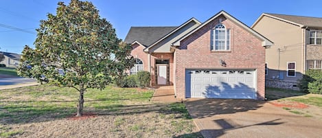 A single-story brick house with a white garage door, a small front porch, and a tree in the front yard.