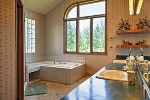 Une salle de bain avec une baignoire, un lavabo et une fenêtre donnant sur les arbres.