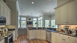A modern kitchen with white cabinets, a central island, and a large window providing natural light. - Upscale Palm Coast Home w/ Pool: 7 Mi to Beaches! (Palm Coast)