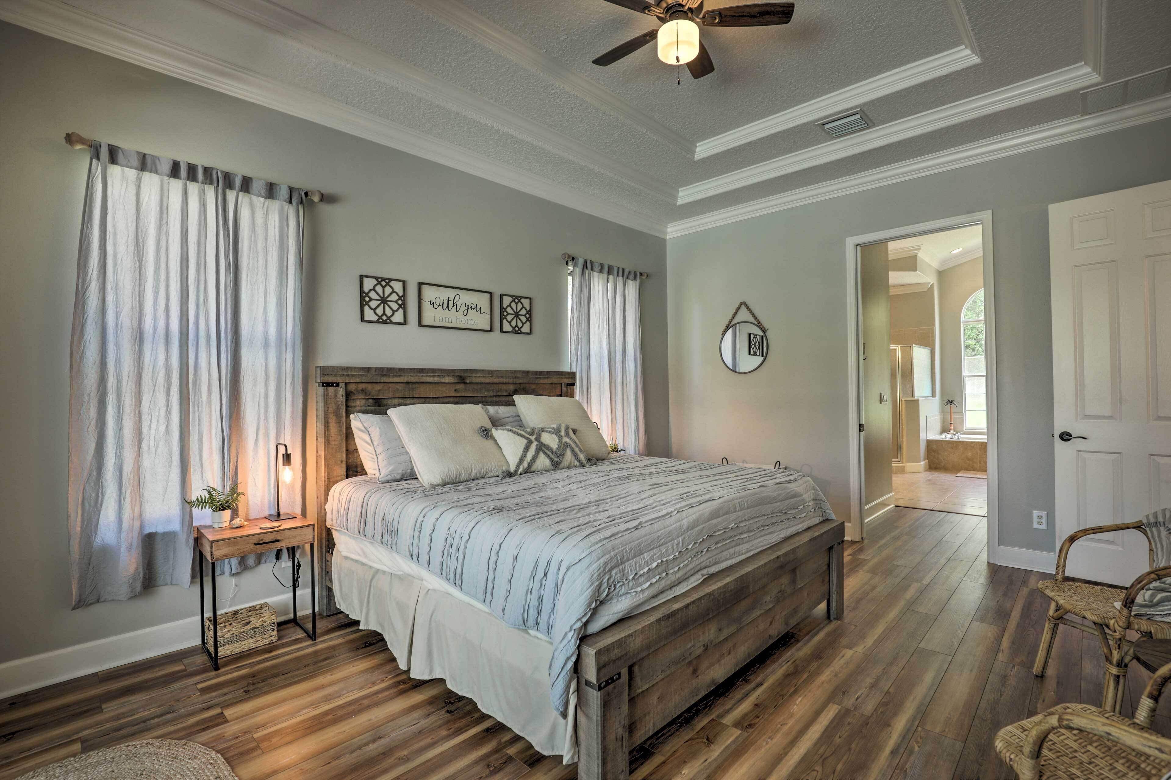 A bedroom with a wooden bed, a nightstand, a ceiling fan, and a view into another room.