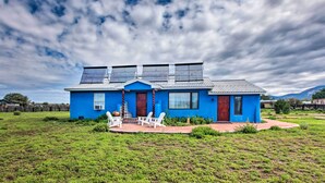 A blue house with solar panels on the roof, a patio with chairs, and a grassy yard. - Cozy 'blue Adobe' w/ Steam Room 2 Mi. From Taos! (El Prado)