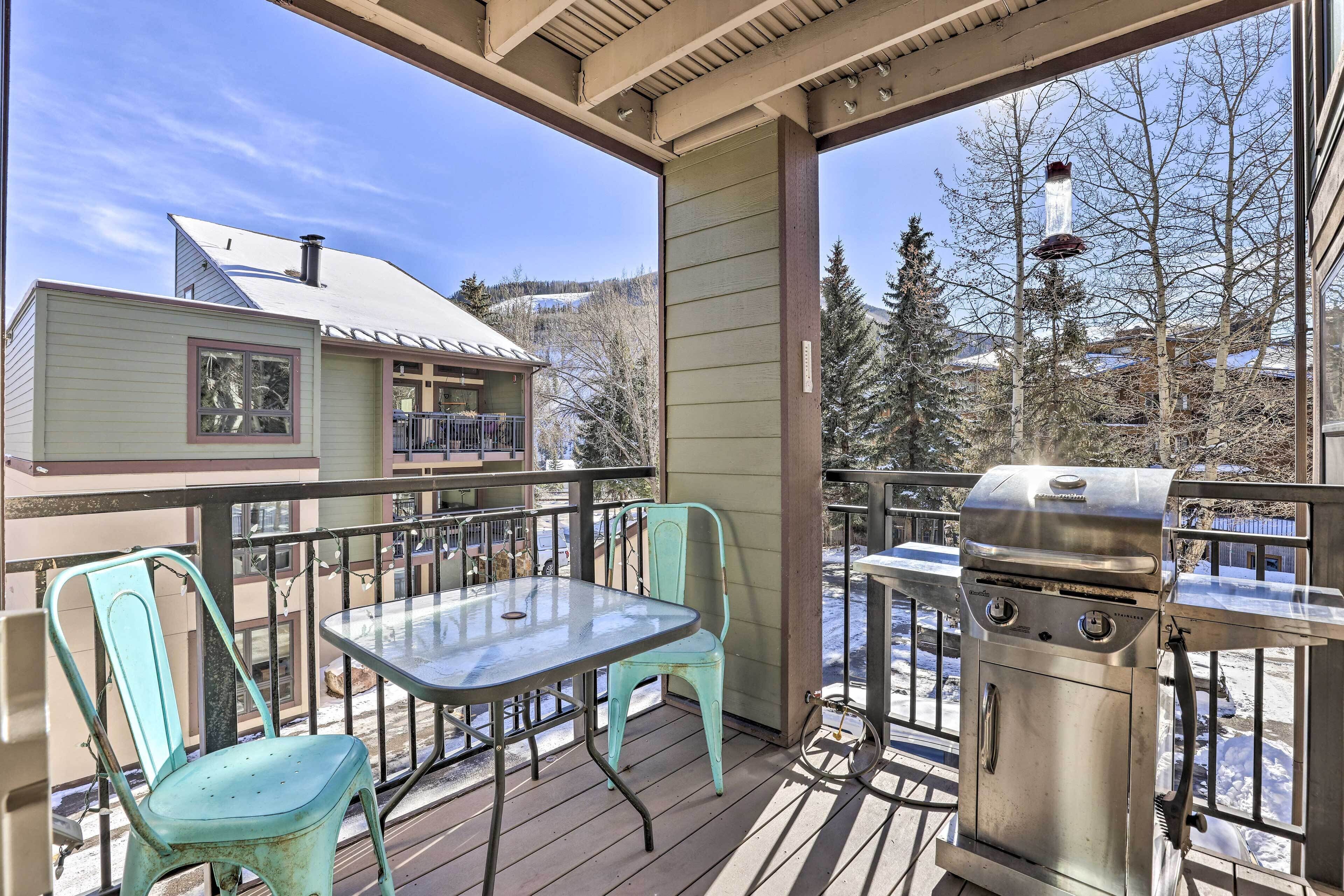 A balcony with a grill, two chairs, and a table.