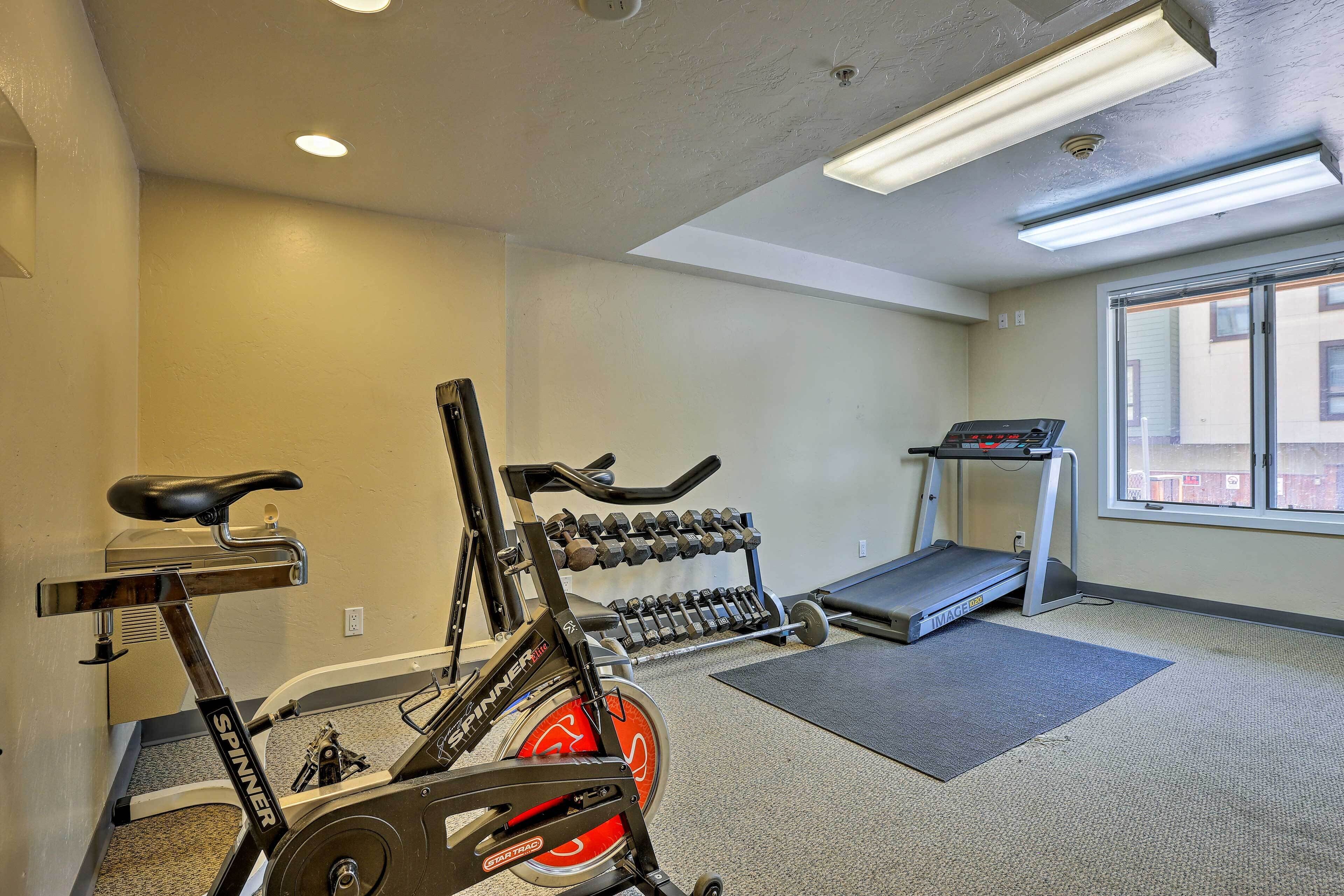 Ein Fitnessraum mit Trainingsgeräten, darunter ein Ergometer, Kurzhanteln und ein Laufband.