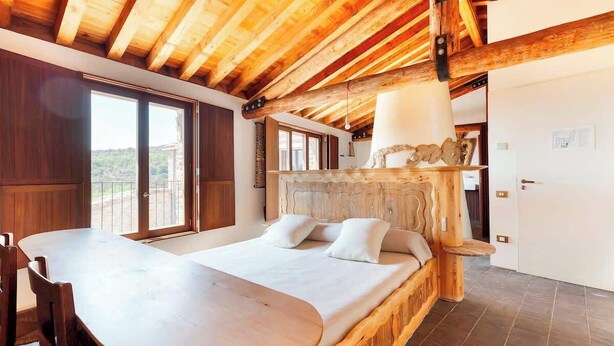 A bedroom with a wooden bed, a dining table, and a large window. - Casa Fumanal - Unique Property for up to 24 (Abizanda)