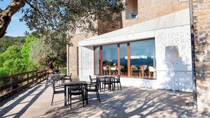 An outdoor patio with tables and chairs, a stone wall, and a view of the sea. - Casa Fumanal - Unique Property for up to 24 (Abizanda)