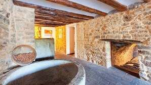 A rustic stone interior with exposed wooden beams, a stone fireplace, and a stone bench with a bowl of nuts. - Casa Fumanal - Unique Property for up to 24 (Abizanda)