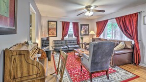 A living room with a ceiling fan, a red and white patterned rug, a wooden piano, a black leather sofa, and a brown leather armchair.