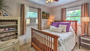 A bedroom with a wooden crib, a ceiling fan, and a window with curtains.