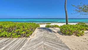 Een houten pad dat naar een strand leidt met helder turquoise water en een palmboom.