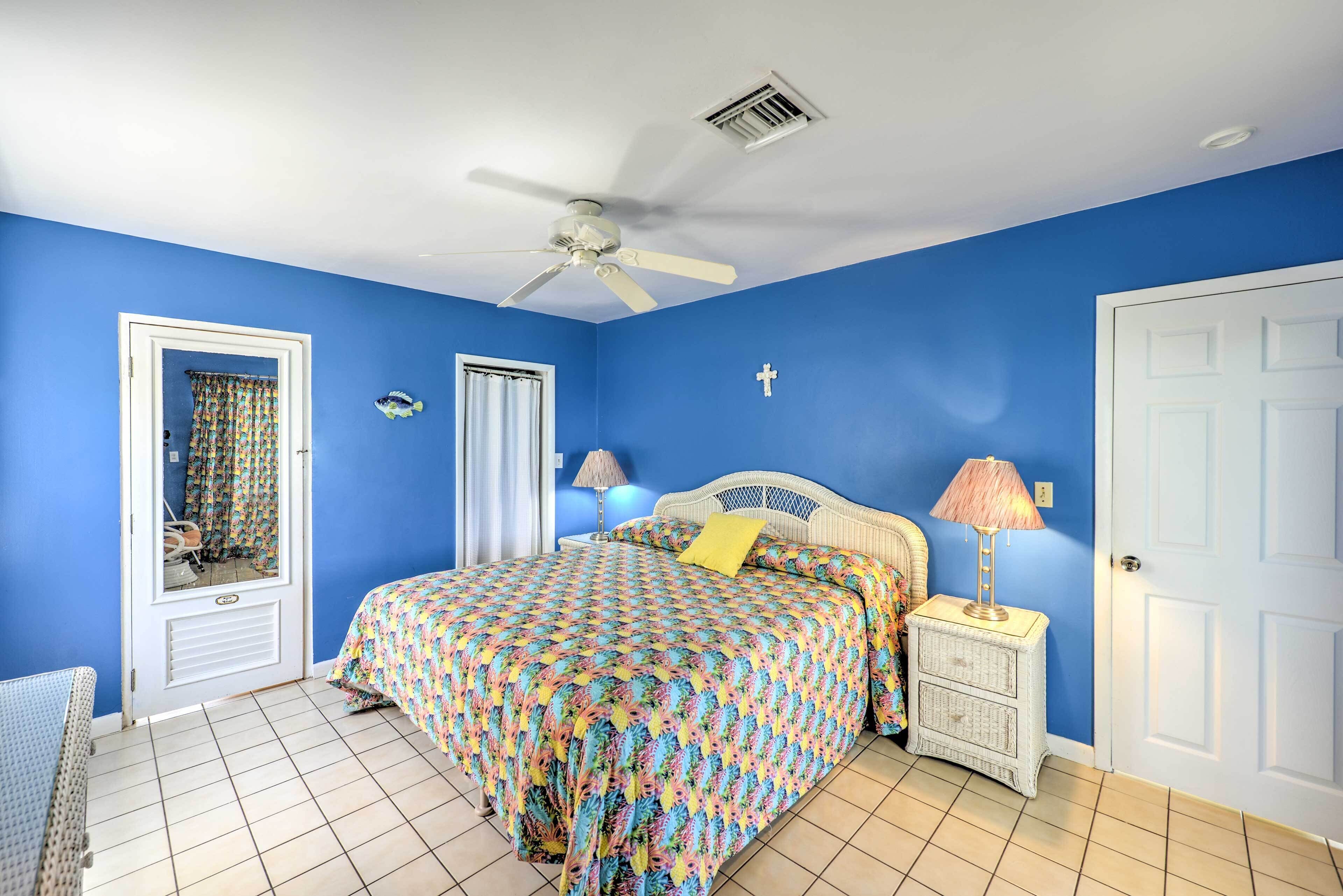 A bedroom with a bed, a ceiling fan, a nightstand with a lamp, and a door.
