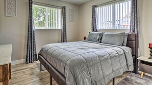 Une chambre à coucher avec un lit, des rideaux, un ventilateur de plafond et une fenêtre avec des stores.