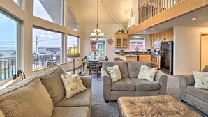 A spacious living room with large windows, a dining area, and a kitchen with wooden cabinets and a black refrigerator. - Logan Road Lookout, Lincoln City Home w/ Game Room (Lincoln City)