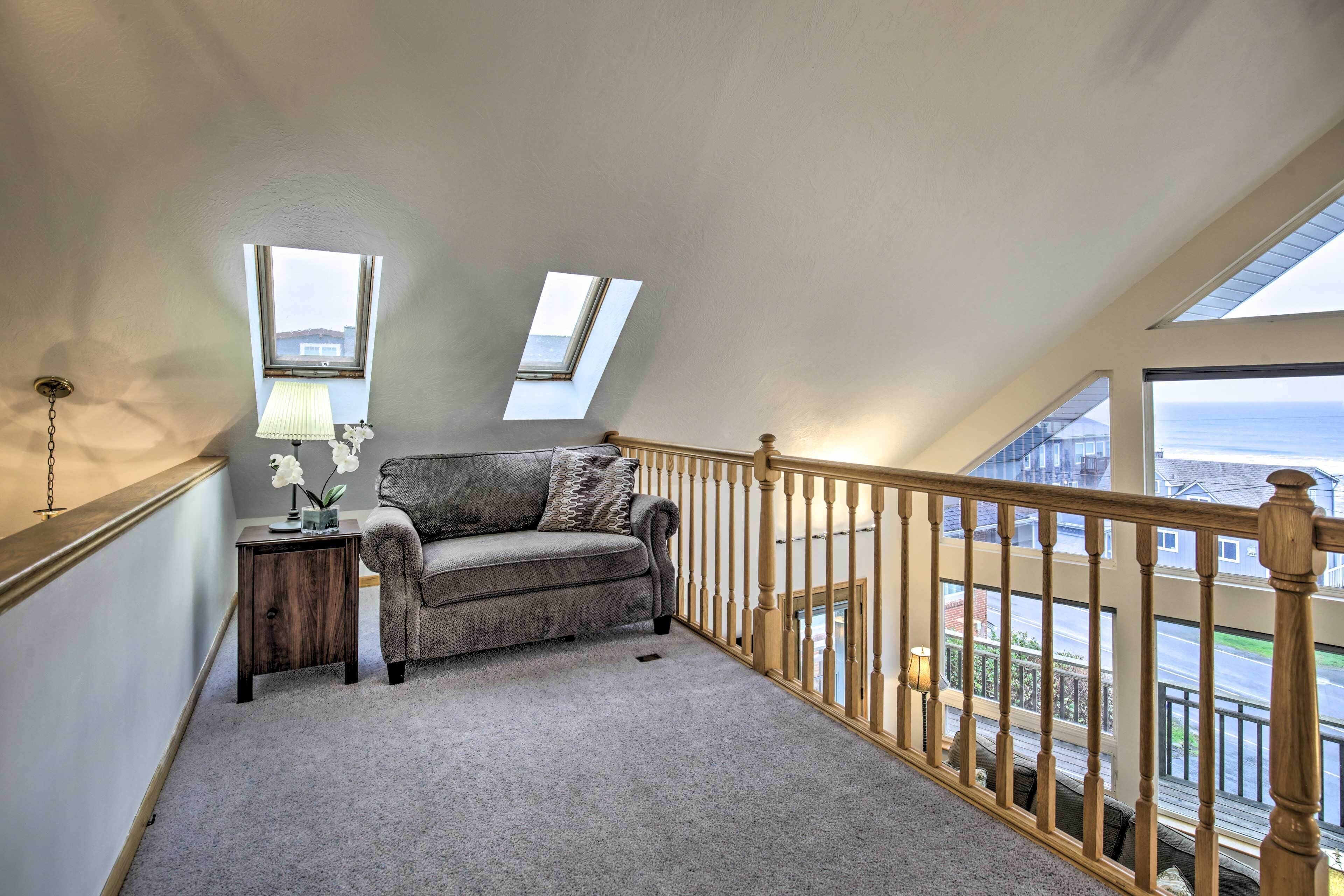 Ein Schlafzimmer im Loft-Stil mit grauem Sofa, einem kleinen Beistelltisch mit Lampe und Blick durch große Fenster.