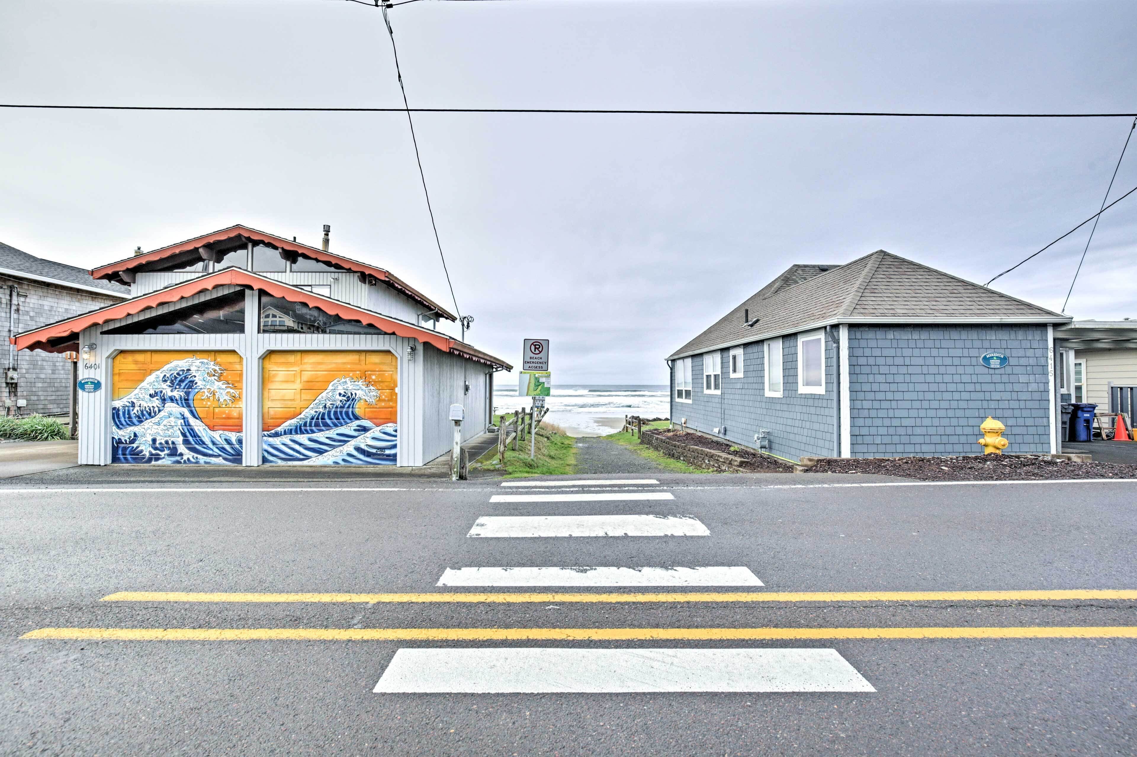 A street with a pedestrian crossing and buildings on either side, one with a mural and another with a blue exterior.