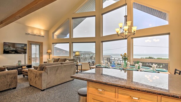 A spacious living area with a large window overlooking a balcony, a kitchen with granite countertops, and a cozy seating area with a sofa and armchairs. - Logan Road Lookout, Lincoln City Home w/ Game Room (Lincoln City)