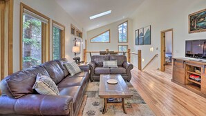 A spacious living room with leather sofas, a coffee table, and a wooden cabinet. Large windows provide natural light and views of the outdoors. - Creekside Mtn House w/ Deck: 8 Mi to Idaho Springs (Dumont)