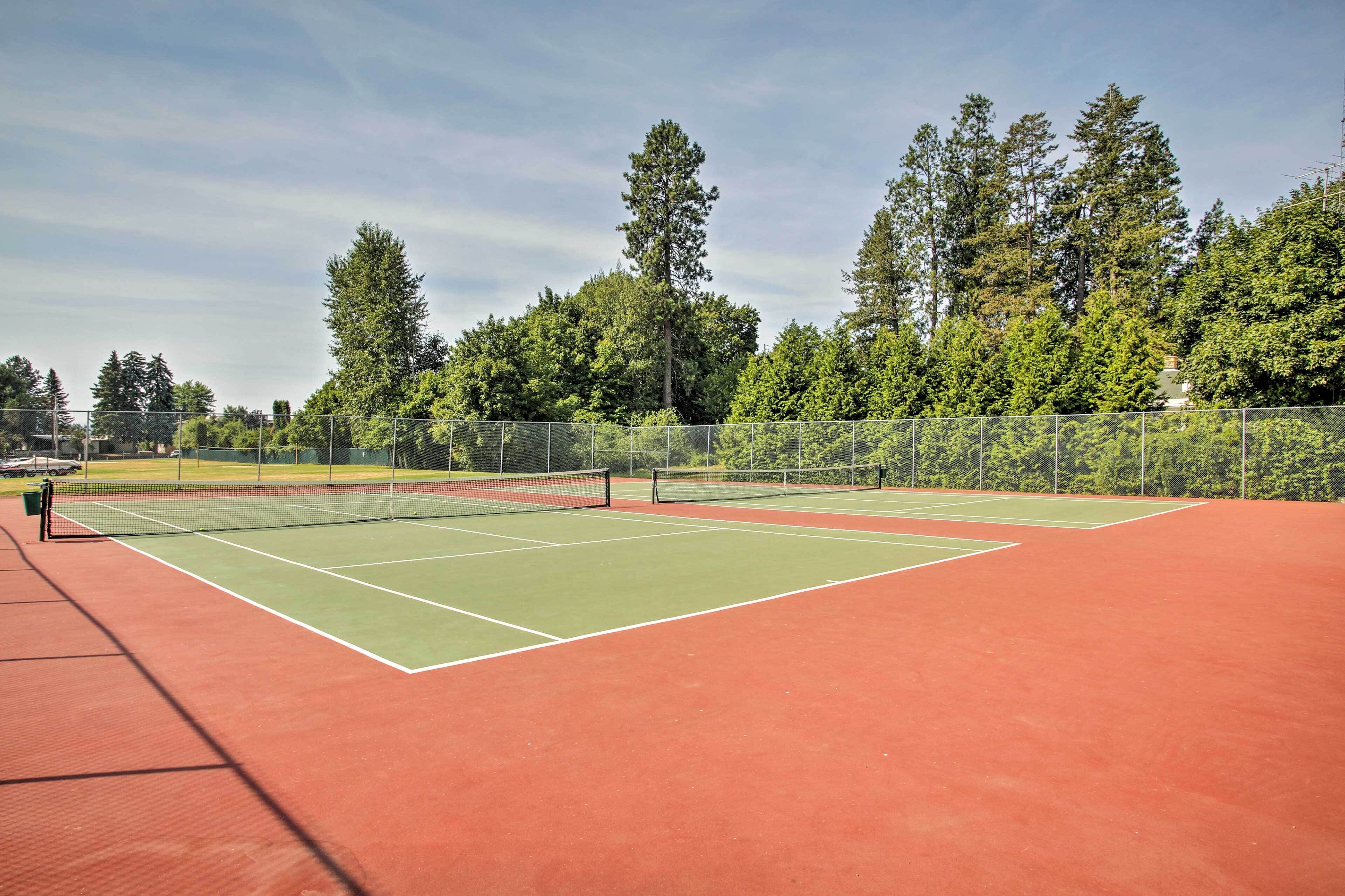 A tennis court with a net, surrounded by trees and a fence.