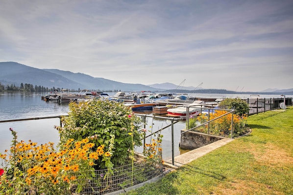 A marina with boats docked, a grassy area with flowers, and mountains in the background.
