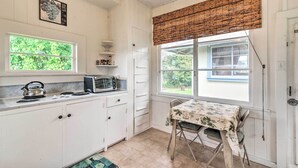Une cuisine compacte avec des meubles blancs, une petite table et une fenêtre donnant sur un espace verdoyant.