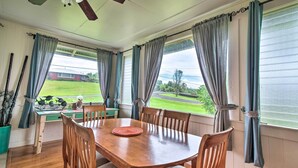Un espace repas avec une table et des chaises en bois, une vue sur un paysage verdoyant et un ventilateur de plafond.