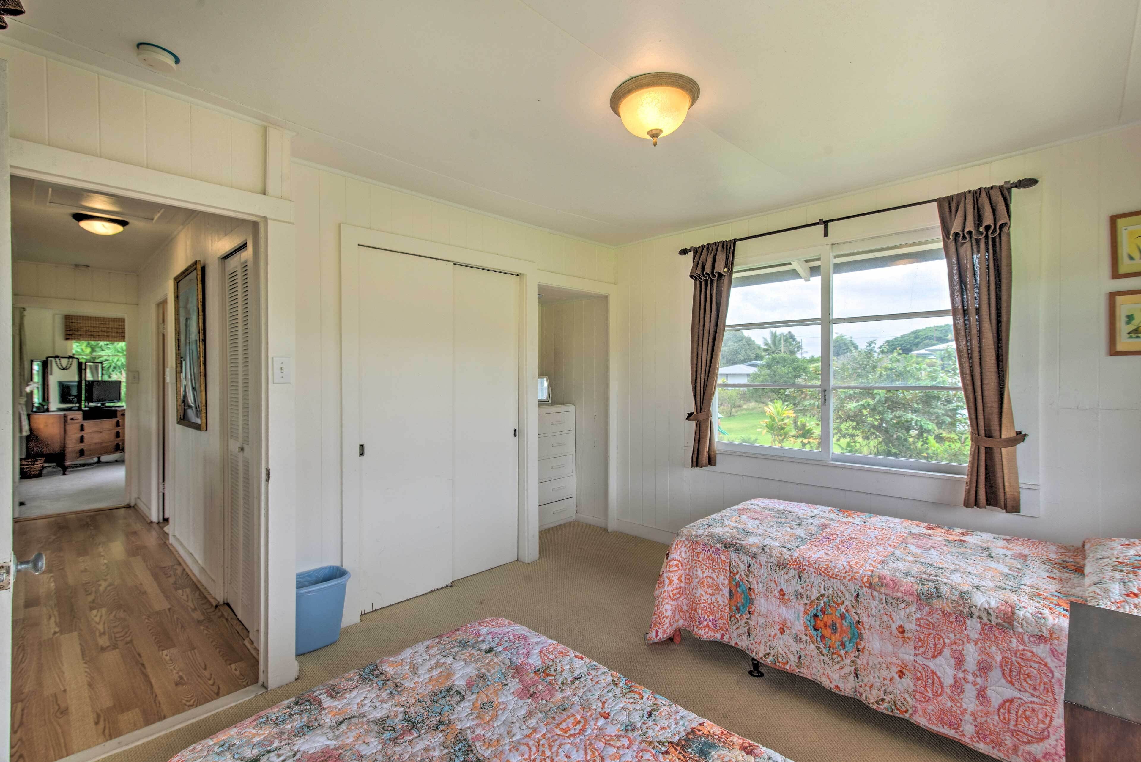 A room with two beds, a window with curtains, a door, and a hallway leading to another room.