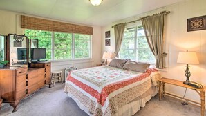 Une chambre à coucher comprenant un lit, une commode, un téléviseur et une fenêtre avec des rideaux.