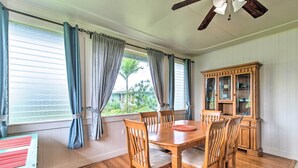 Un coin repas avec une table et des chaises en bois, un buffet et une vue sur les palmiers à travers les fenêtres.
