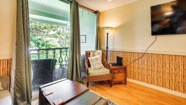 A room with a wooden floor, a dining table, a chair with a cushion, a lamp, and a TV mounted on the wall. - Kailua-kona Islander Studio: Lanai, Community Pool (Kailua-Kona)