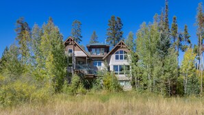 A two-story house with a balcony and a large window, surrounded by tall trees and a grassy field. - Mountain Home ~ 5 Mi to Winter Park Resort! (Winter Park)