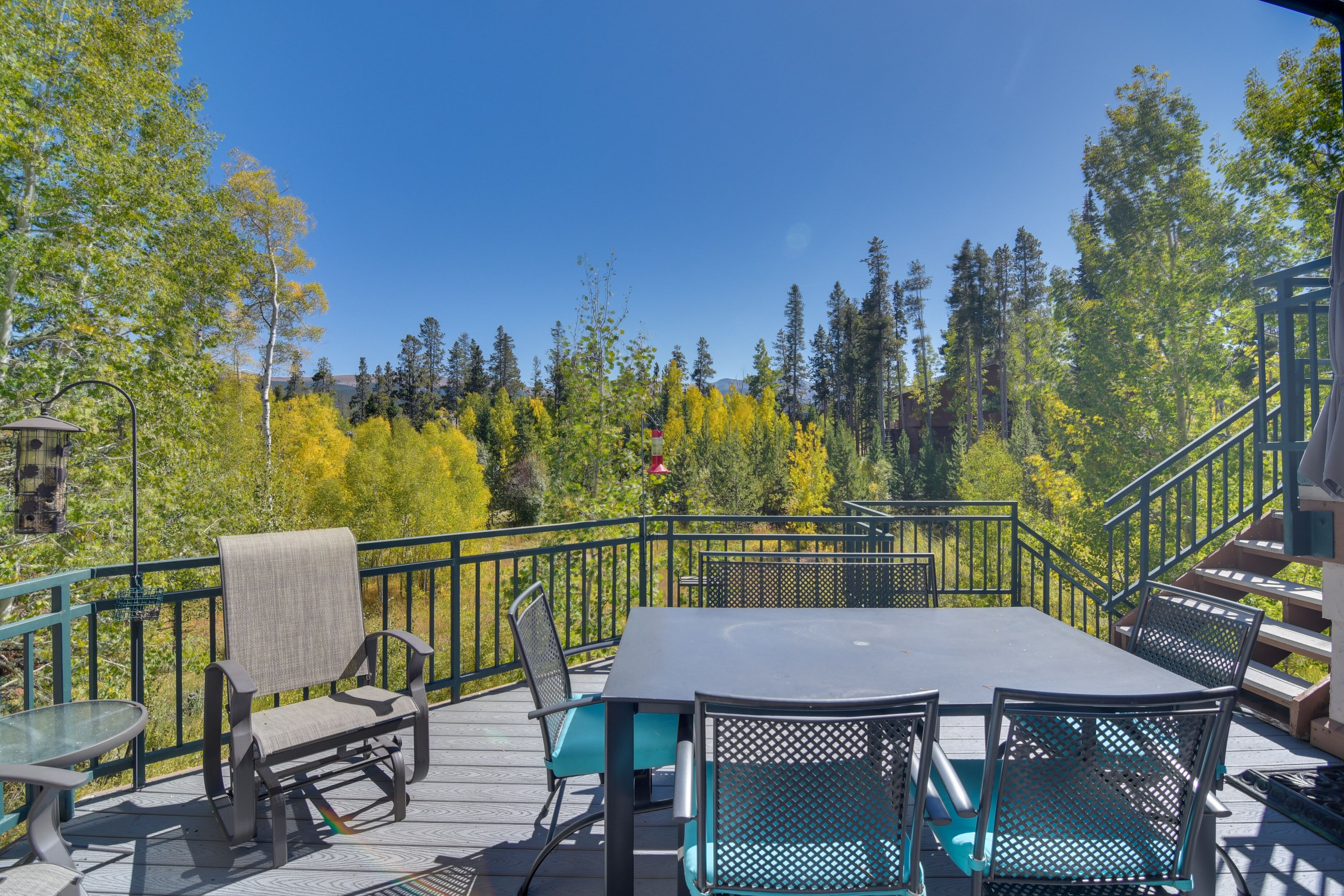 An outdoor deck with a table and chairs, surrounded by a metal railing and trees.