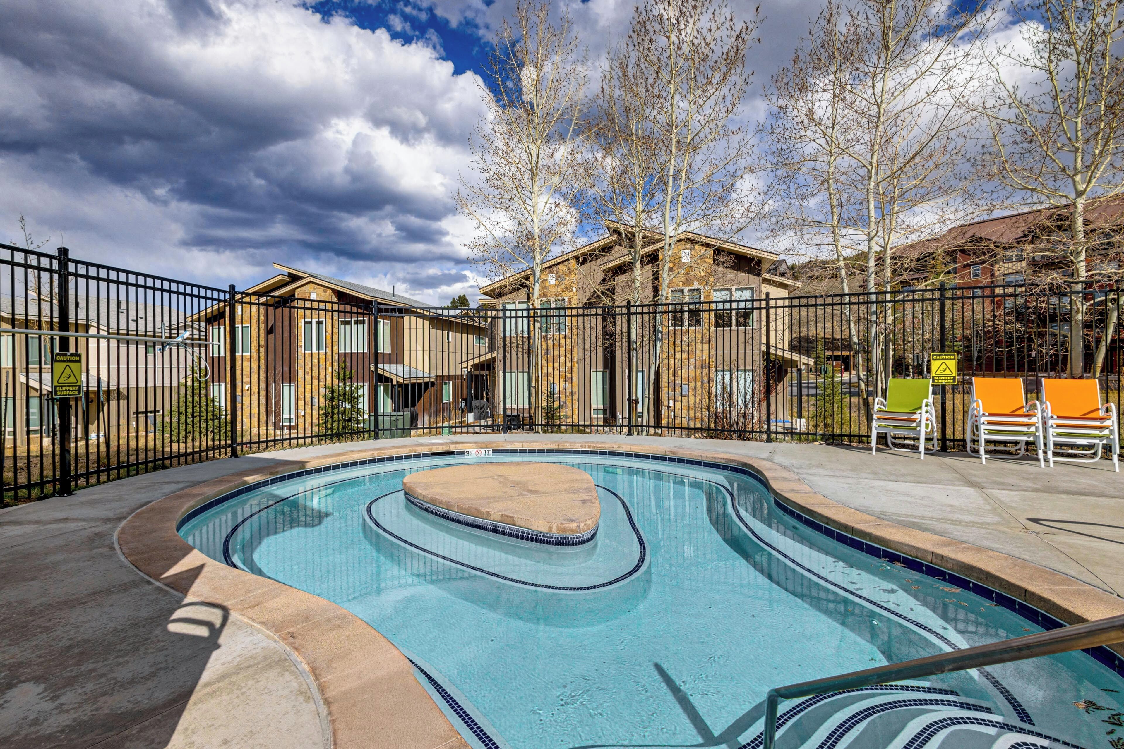 A swimming pool with a curved design, surrounded by a fence, and adjacent to a building with a brick facade.