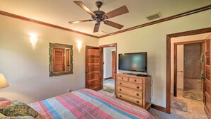Ein Schlafzimmer mit Bett, Schminktisch, Deckenventilator, Fernseher und Duschbereich.