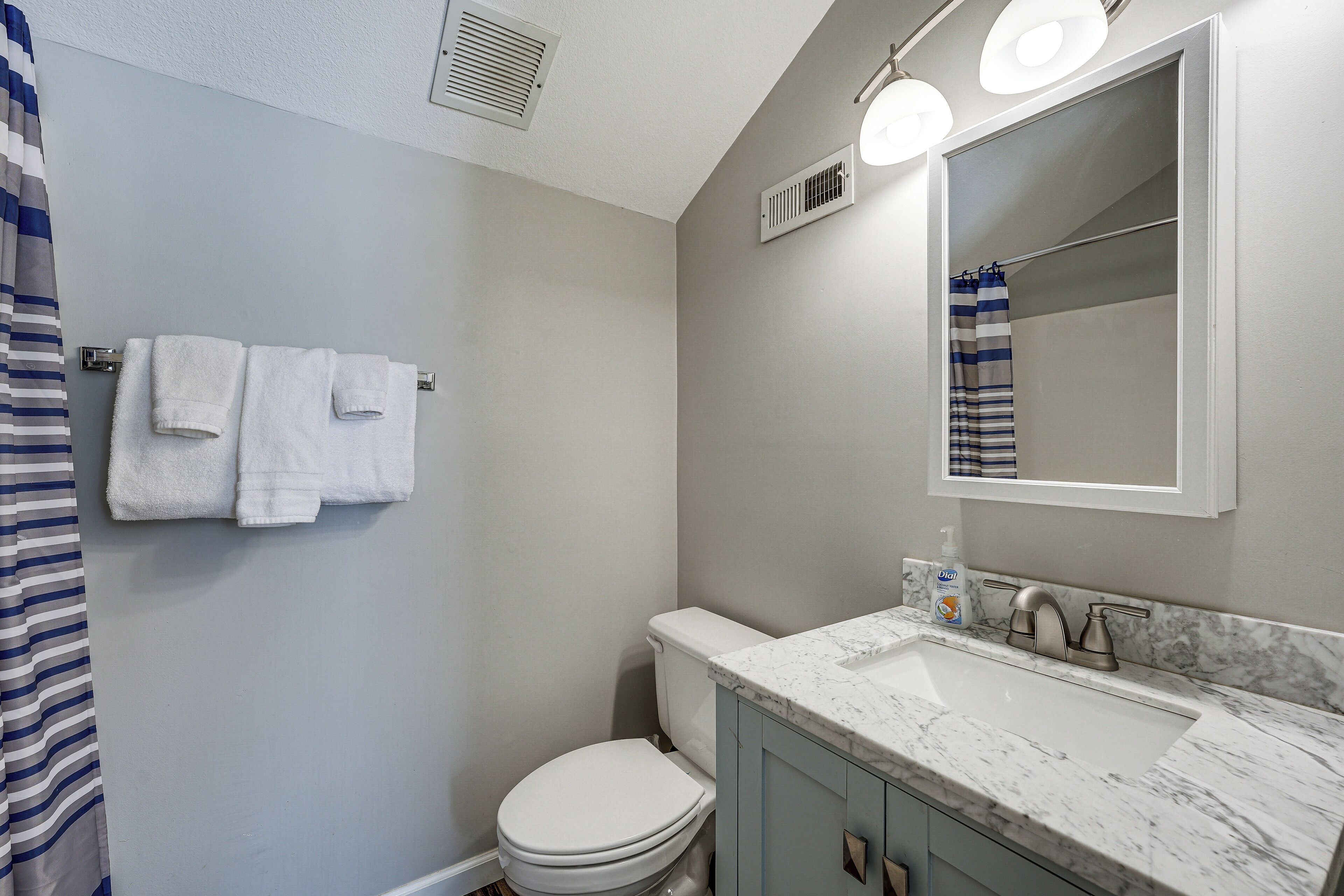 A bathroom with a white toilet, a marble sink, and a striped shower curtain.