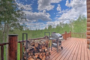 A wooden deck with a grill and firewood, surrounded by trees and a grassy area. - 22str-00506 Fairplay Log Cabin: 26 Mi to Breck! (Fairplay)