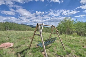 Un conjunto de columpios de madera en un campo con césped, árboles y montañas al fondo.