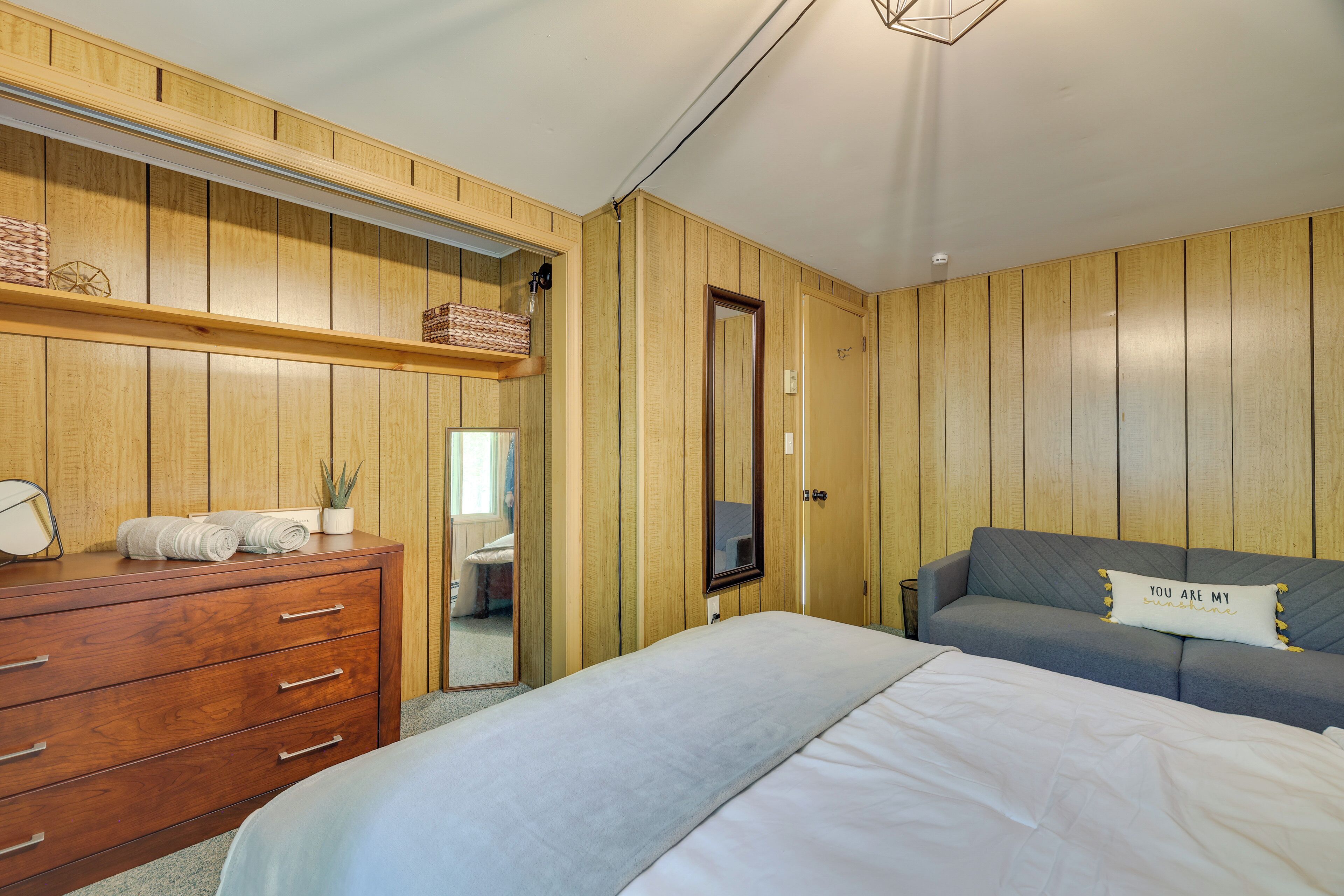 Une chambre avec une armoire en bois, un lit, un canapé gris et un miroir.