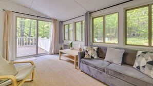 A spacious living room with a grey sofa, a wooden coffee table, and a view of a balcony with a white fence.