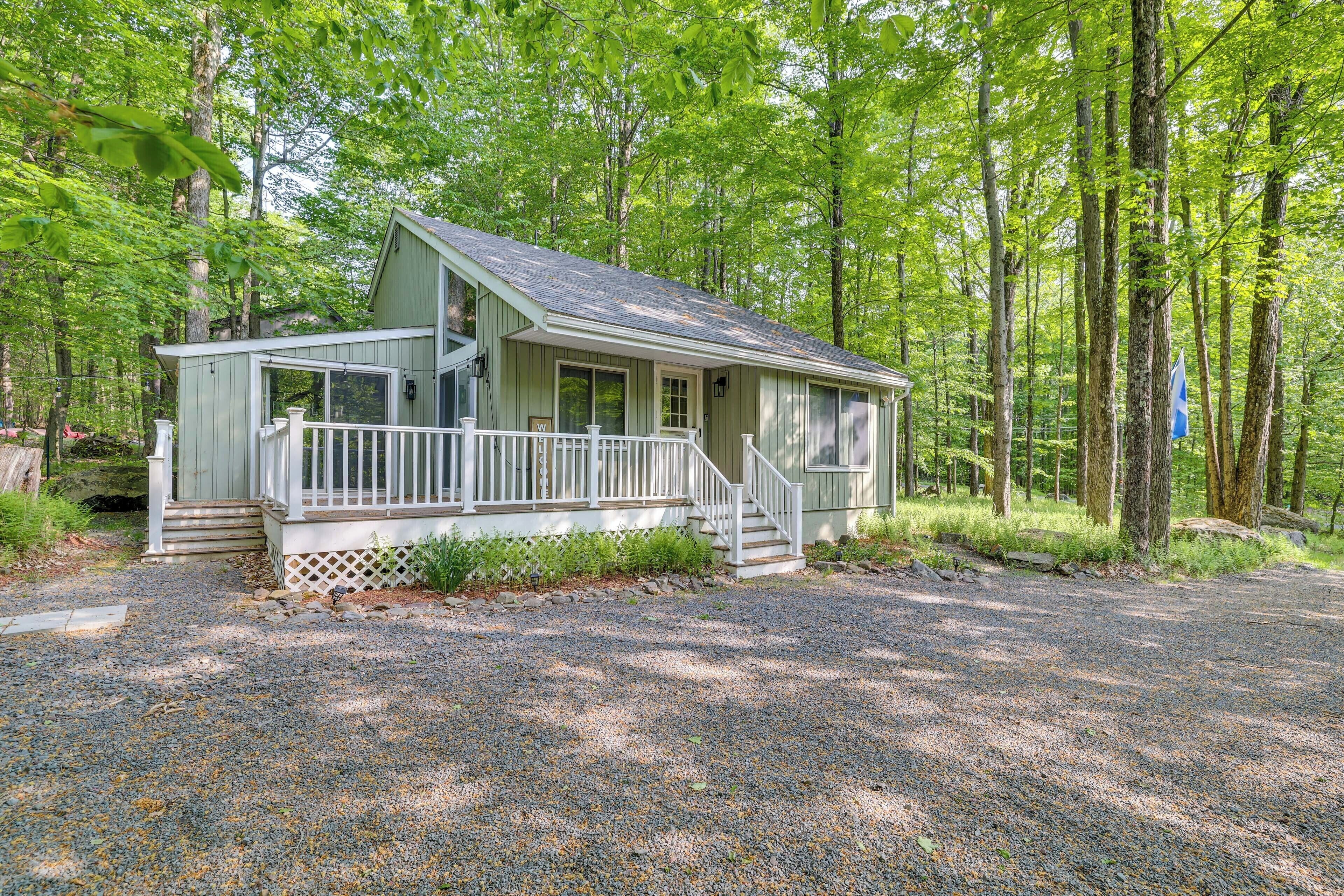 A small, single-story cabin with a porch and steps, surrounded by a forest.